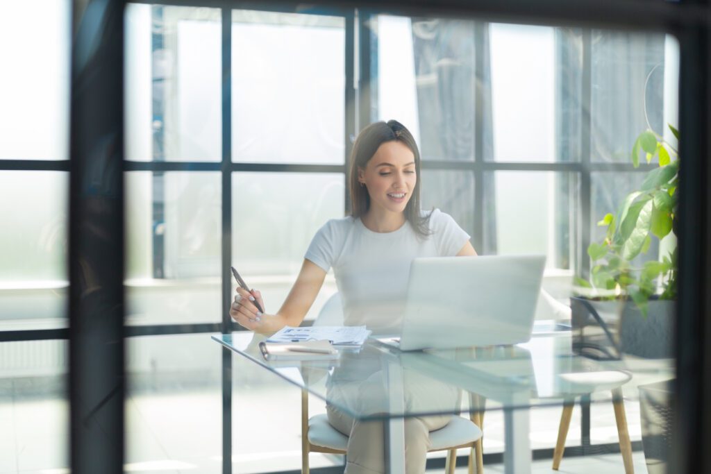 Beautiful caucasian business woman is working using digital tablet while sitting in creative office. The view is through the glass Canadian digital adoption program